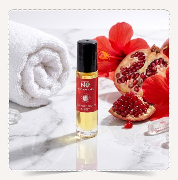 زيت الجسم شيني (Shiny Body Oil) برائحة الرمان والزهور على سطح رخامي مع كريستالات لامعة.
