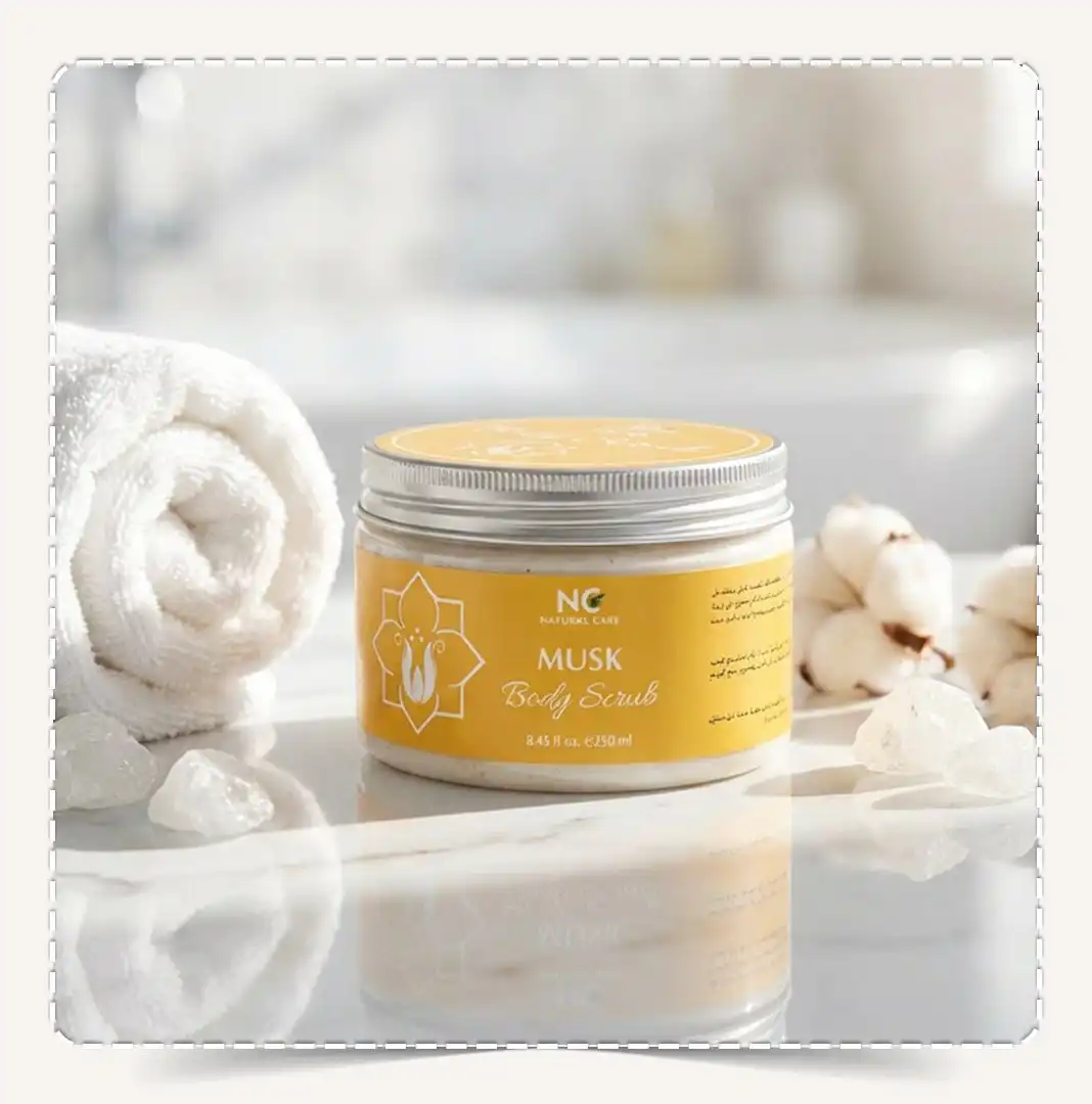عبوة مقشر الجسم مسك Musk Body Scrub صفراء على سطح رخامي مع منشفة وقطن وأحجار مسك بيضاء.