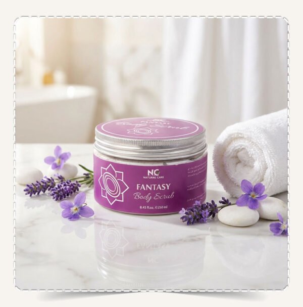 عبوة مقشر الجسم فانتسي Fantasy Body Scrub بنفسجية على سطح رخامي مع منشفة وزهور برية وأحجار بيضاء.