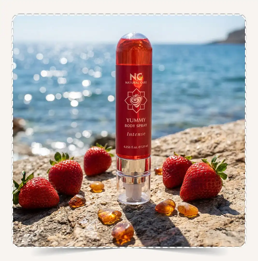 معطر الجسم يمي Yummy Body Spray على صخرة شاطئية مع البحر في الخلفية وفراولة طازجة.