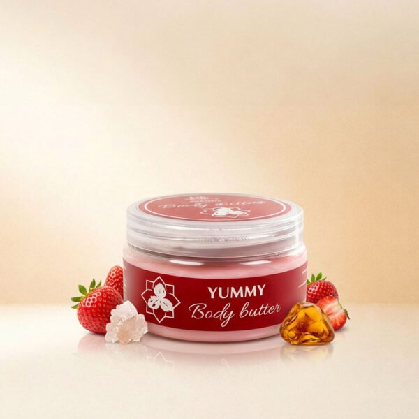 صورة إعلانية تعرض أفضل زبدة الجسم يمي Body Butter Yummy من ناتشرال كير عمان، تبرز العبوة الدائرية الشفافة بملصقها العنابي الأنيق محاطة بحبات الفراولة الطازجة، حجر العنبر الدافئ، وبلورات السكر والأملاح الطبيعية على سطح زجاجي عاكس.