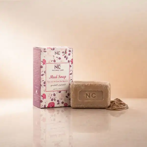عبوة وقطعة صابون الطين بأملاح البحر الميت | Mud Soap من ناتشرال كير عمان، بجوار عينة من طين البحر الميت الخام لتعكس قوة التنظيف العميق ومعادن البحر الميت.