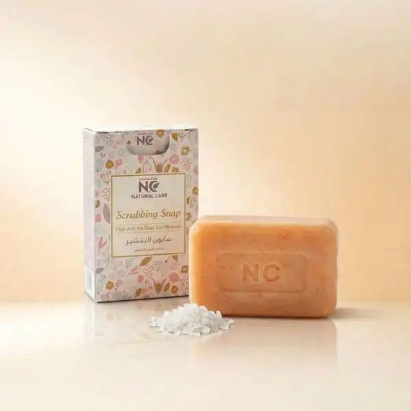 صندوق وقطعة صابون التقشير بأملاح البحر الميت | Scrub Soap من ناتشرال كير عمان، بجوار بلورات أملاح البحر الميت النقية لتعكس قوة التقشير الطبيعي وتجديد خلايا البشرة.