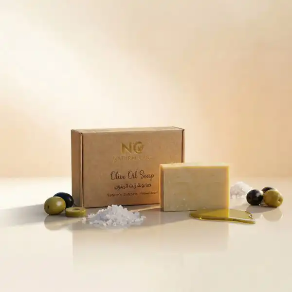 صندوق وقطعة صابونة زيت الزيتون الطبيعية - Olive Oil Soapمن ناتشرال كير عمان، محاطة بحبات الزيتون الطازجة وزيت الزيتون الذهبي وأملاح البحر الميت لتعكس النعومة الفائقة.