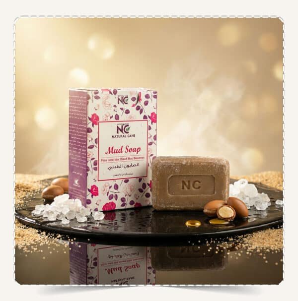 صابون الطين بأملاح البحر الميت | Mud Soap من ناتشورال كير عمان Natural Care Oman — عبوة Mud Soap مع قالب الصابون وأملاح البحر الميت وخلفية ذهبية