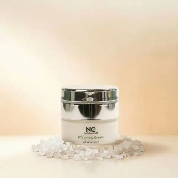 عبوة كريم تفتيح البشرة وتوحيد اللون Whitening Cream من ناتشرال كير عمان، محاطة ببلورات أملاح البحر الميت البيضاء النقية التي تعكس قوة التركيبة الطبيعية الفعالة.