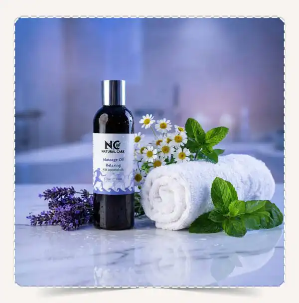 عبوة زيت مساج ريلاكسينج Massage Oil Relaxing الداكنة على سطح رخامي مبلل مع أزهار اللافندر والبابونج ومنشفة بيضاء.