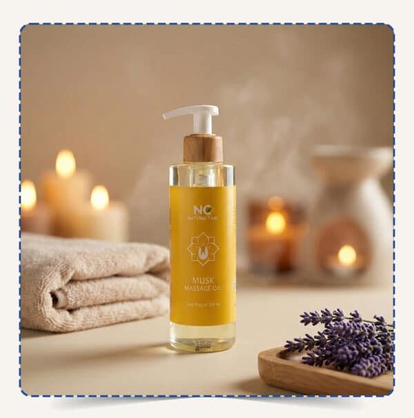 عبوة Musk Massage Oil بتصميم أصفر/ذهبي جذاب مع مضخة خشبية، محاطة بالمناشف والشموع وزهور اللافندر في أجواء سبا فاخرة – ناتشورال كير عمان
