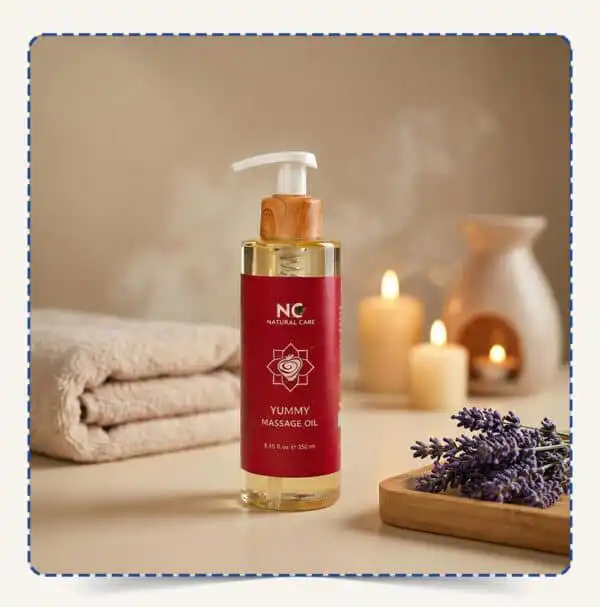 عبوة Yummy Massage Oil بتصميم أحمر وجذاب مع مضخة خشبية، محاطة بالمناشف والشموع وزهور اللافندر في أجواء سبا دافئة – ناتشورال كير عمان