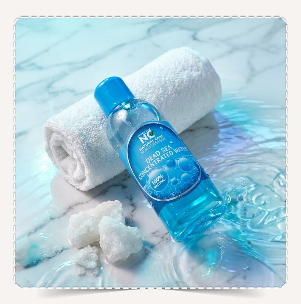 زجاجة زيت المغنيسيوم Magnesium Oil من Natural Care على سطح رخامي مع منشفة وبلورات ملح البحر الميت وتأثير تموجات الماء.