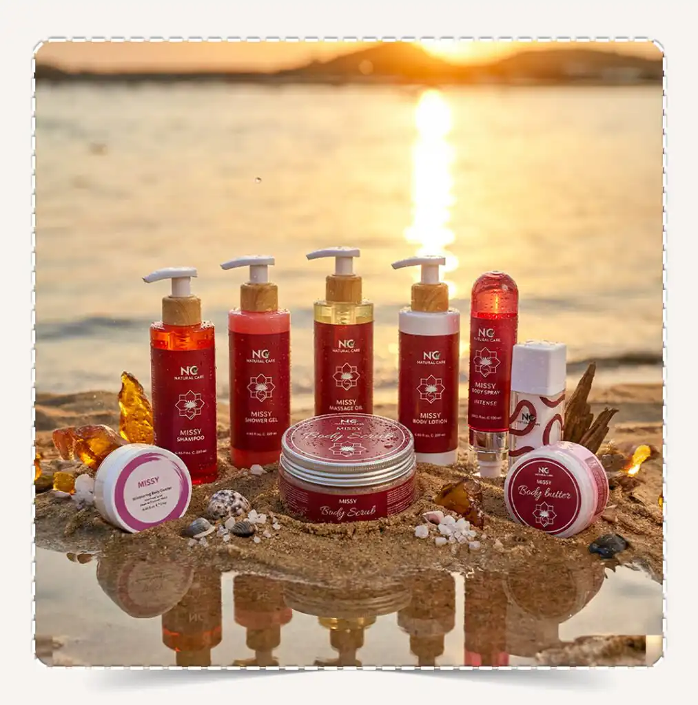 منتجات مجموعة ميسي | Missy Collection للعناية بالجسم برائحة العنبر والعود والمسك معروضة على رمال الشاطئ مع انعكاس ضوء الغروب.