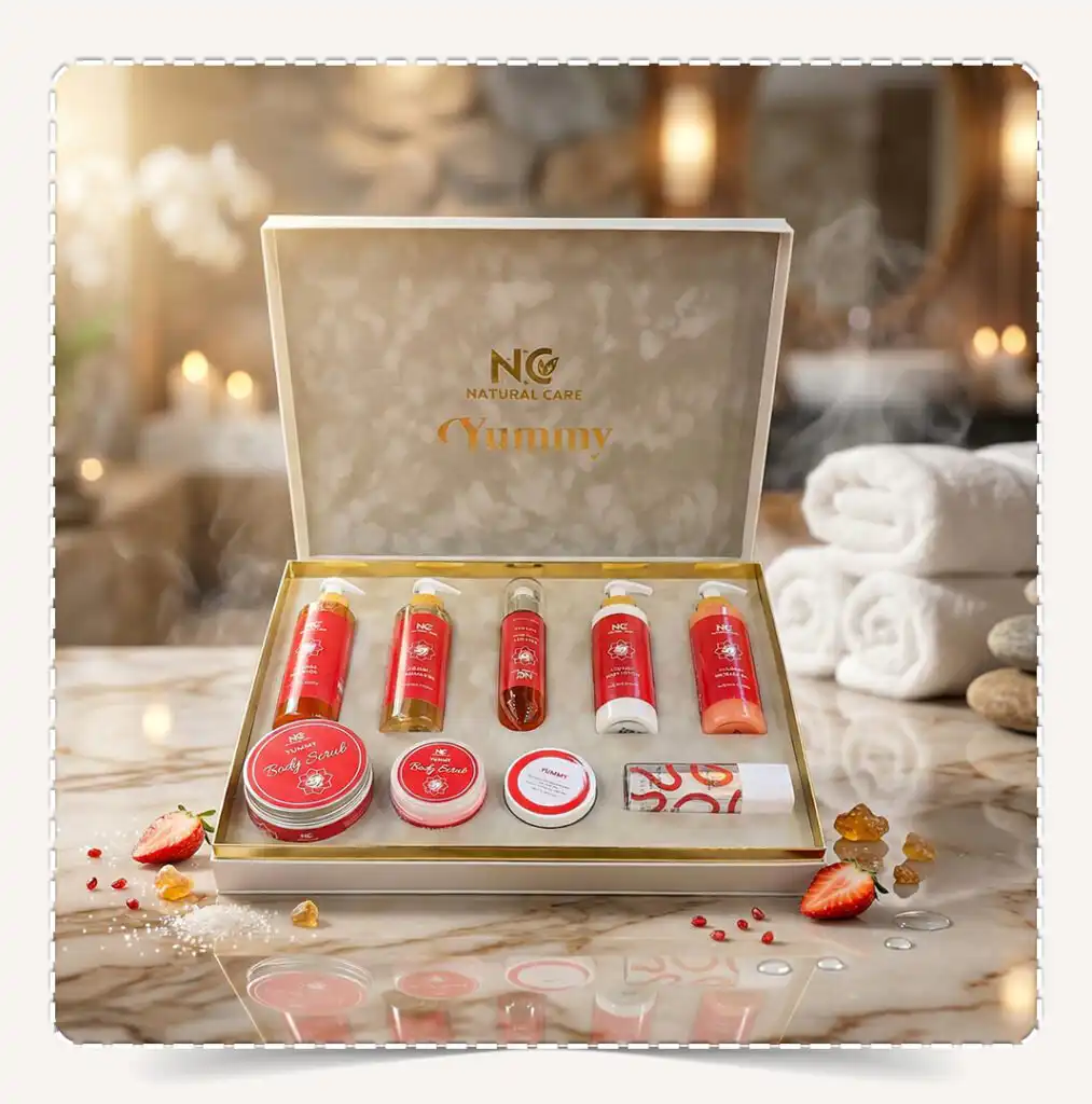 صندوق مجموعة يامي | Yummy Collection المفتوح بعبواته الحمراء الفاخرة على رخام أبيض في أجواء سبا دافئة مع قطع الفراولة الطازجة وأحجار العنبر.