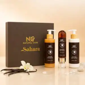 عبوة ومنتجات مجموعة العناية اليومية صحارى من ناتشرال كير عمان، صندوق فاخر يحتوي على ثلاثة منتجات: لوشن للجسم، معطر جسم مركز، وجل استحمام، محاطة بزهرة الفانيليا وأحجار المسك الأبيض.
